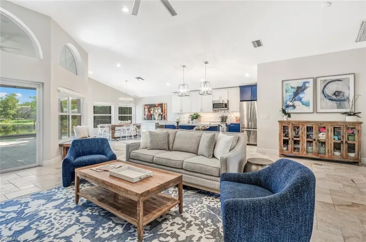 Living room featuring ceiling fan with notable chandelier, light tile patterned floors, and lofted ceiling