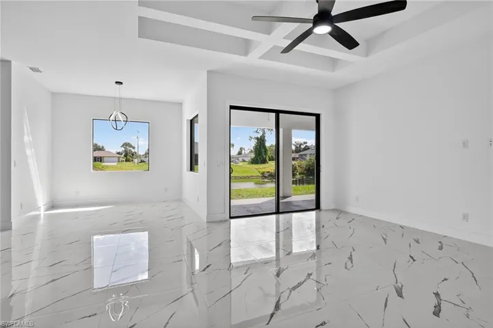 Spare room featuring coffered ceiling, plenty of natural light, light marble finish flooring, beamed ceiling, and a ceiling fan
