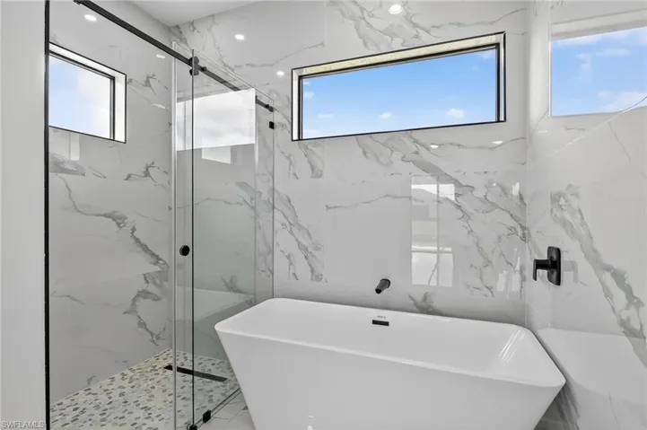 Primary Bathroom with a soaking tub, a marble finish shower, and stone wall