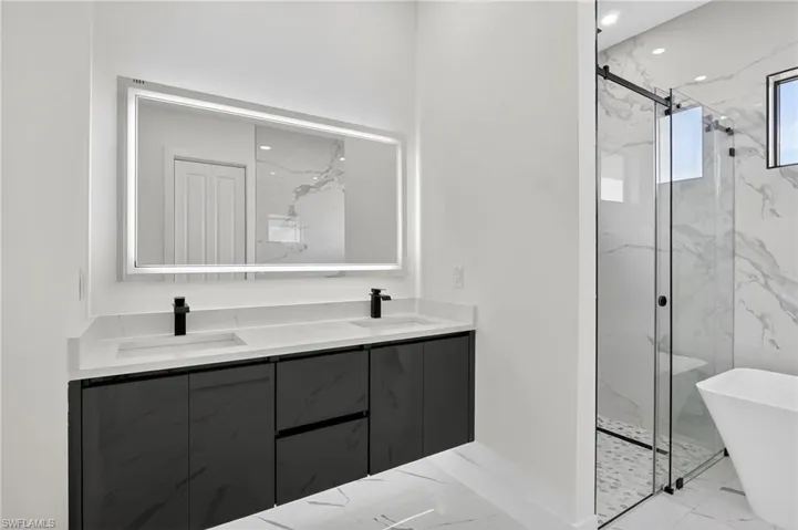 Primary Bathroom with a marble finish shower, light marble finish floors, a freestanding bath, and double vanity