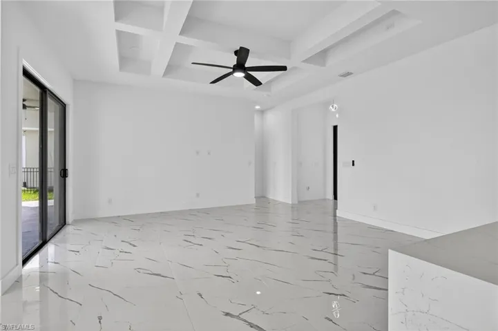 Empty room with coffered ceiling, light marble finish flooring, beamed ceiling, and a ceiling fan