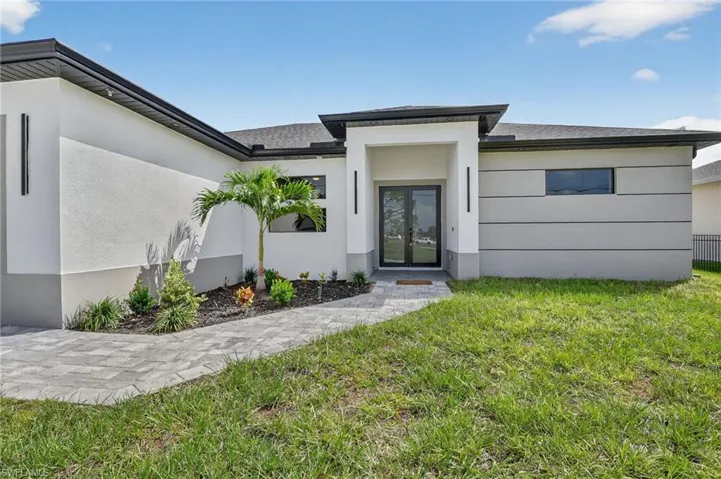 Entrance to property with a lawn, stucco siding, french doors, and roof with shingles