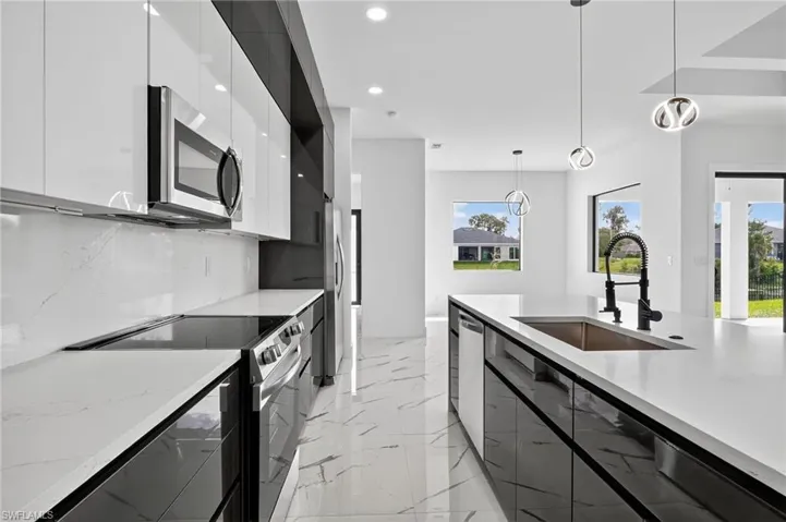 Kitchen with modern cabinets, appliances with stainless steel finishes, decorative light fixtures, light marble finish floors, and light stone countertops