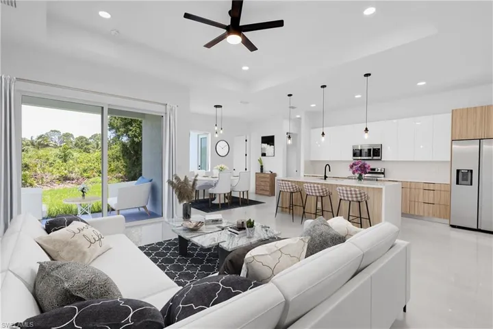 Living room featuring a tray ceiling, sink, light tile flooring, and ceiling fan