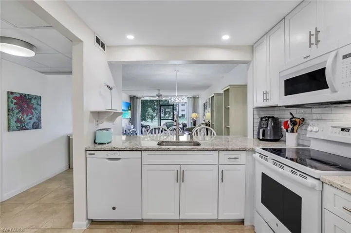 Kitchen featuring white appliances, decorative backsplash, light tile patterned flooring, sink, and white cabinetry