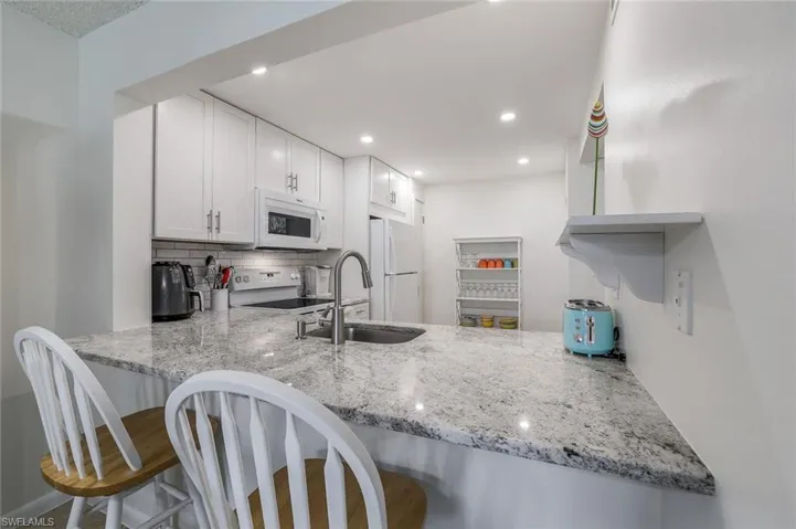 Kitchen with light stone counters, white cabinets, white appliances, and sink
