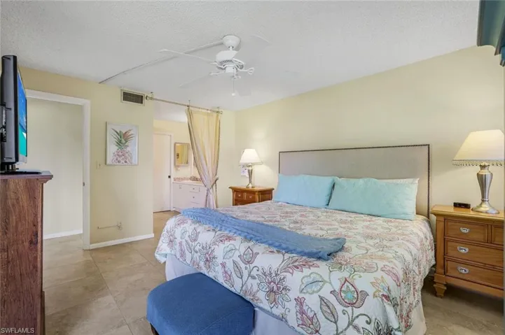 Tiled bedroom with ceiling fan, a textured ceiling, and ensuite bathroom