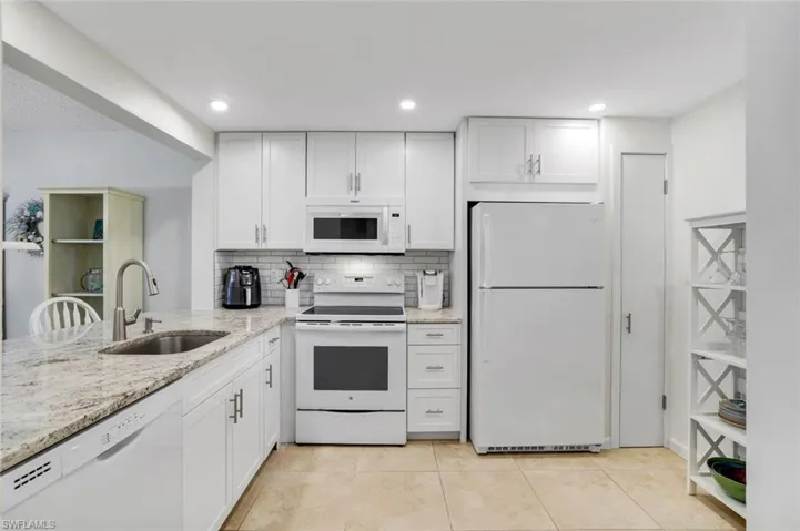 Kitchen with light stone counters, white cabinets, light tile patterned flooring, white appliances, and sink