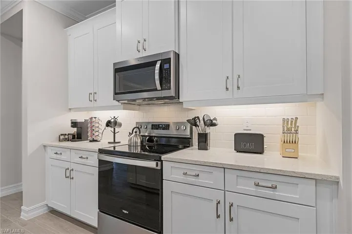 Kitchen featuring white cabinetry, tasteful backsplash, light stone counters, crown molding, and appliances with stainless steel finishes