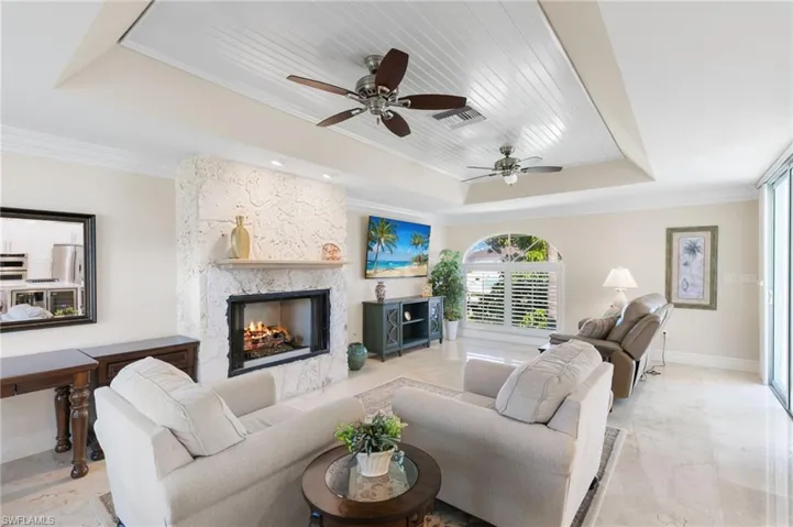 Living area featuring a tray ceiling, ornamental molding, a stone fireplace, and a ceiling fan