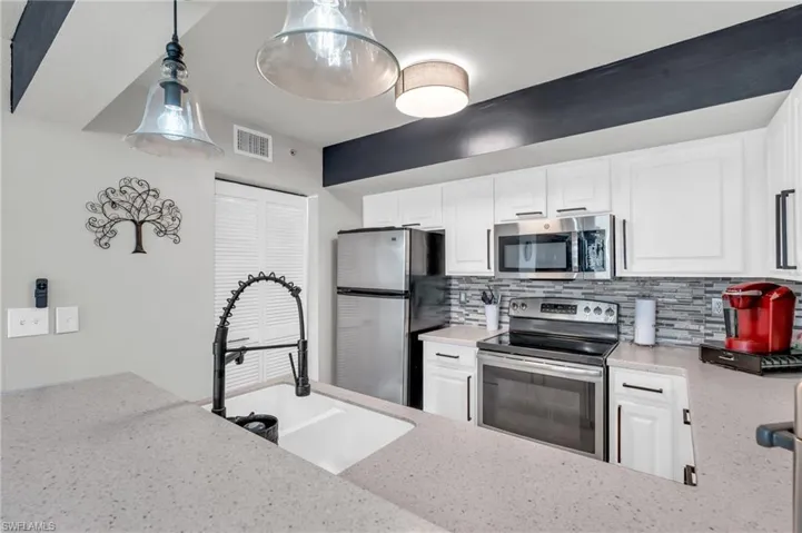Kitchen featuring white cabinetry, stainless steel appliances, sink, backsplash, and hanging light fixtures