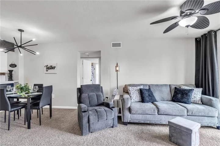 Carpeted living room with ceiling fan with notable chandelier