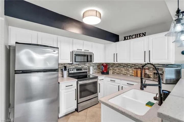 Kitchen with decorative light fixtures, sink, white cabinetry, and appliances with stainless steel finishes