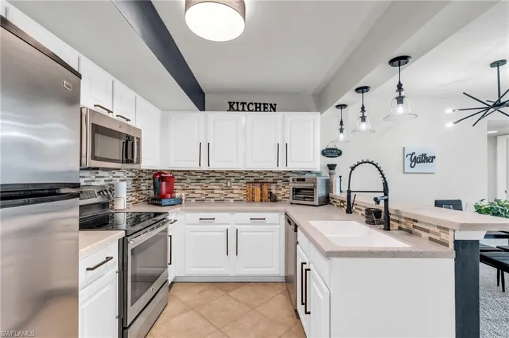 Kitchen with white cabinetry, stainless steel appliances, kitchen peninsula, and sink
