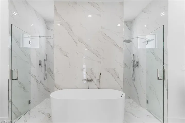 Full bathroom featuring a marble finish shower, a freestanding bath, and stone wall