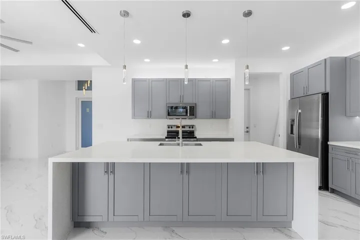 Kitchen with an island with sink, marble finish floor, light countertops, stainless steel appliances, and gray cabinetry