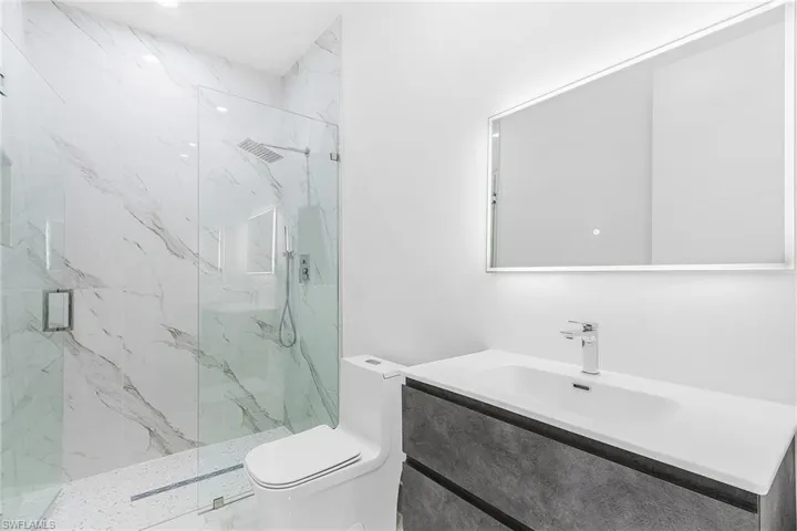 Full bath with toilet, vanity, and a marble finish shower