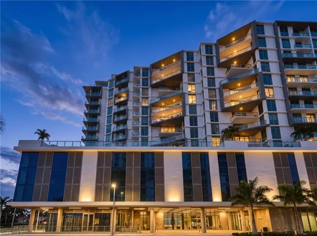 Modern multi-story high-rise exterior featuring glass panel balconies, floor-to-ceiling windows, and recessed architectural lighting