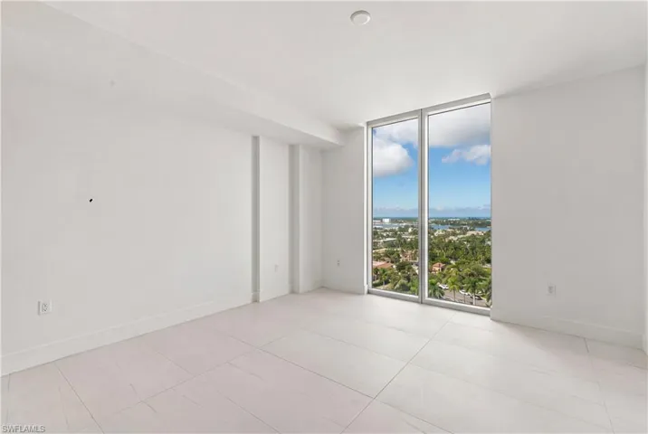 Floor-to-ceiling windows featuring exterior scenery, neutral stone-finish flooring, and crisp white walls
