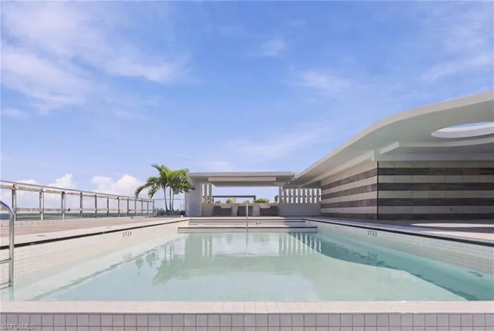 Rooftop pool deck featuring an expansive infinity-edge pool, a covered lounging area, and a railing system