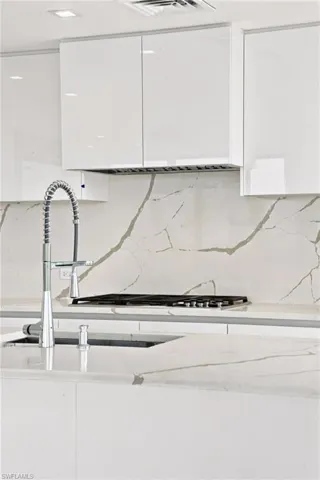 White high-gloss cabinetry, integrated range hood, gas cooktop, sleek countertops, and a contemporary pull-down faucet