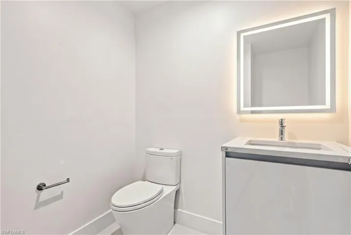 Virtually staged. Guest bath with modern vanity with stone countertop, undermount sink, chrome faucet, and integrated LED backlit mirror, paired with a dual-flush toilet
