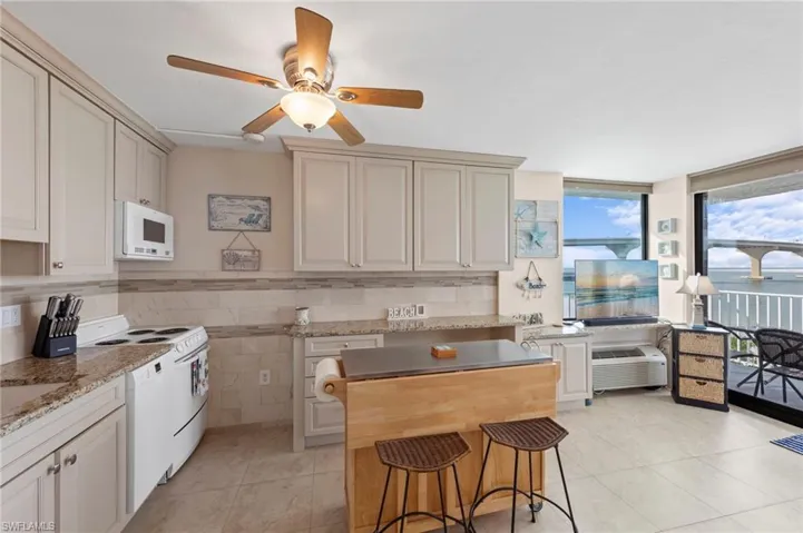 Kitchen featuring white appliances, dark stone countertops, a ceiling fan, light tile patterned floors, and expansive windows