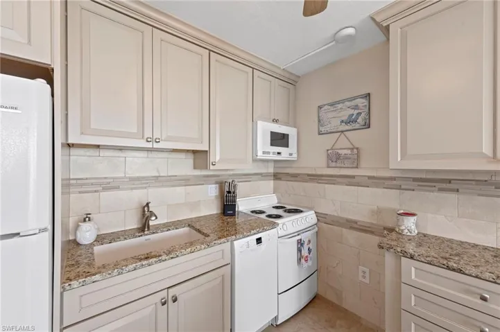 Kitchen featuring white appliances, light stone counters, ceiling fan, and cream cabinetry