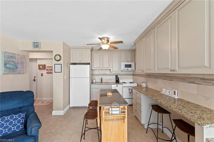 Kitchen with a breakfast bar, white appliances, backsplash, and light tile patterned floors