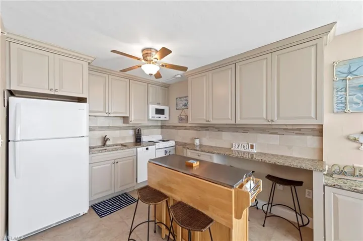 Kitchen with white appliances, light stone countertops, a kitchen breakfast bar, tasteful backsplash, and a ceiling fan