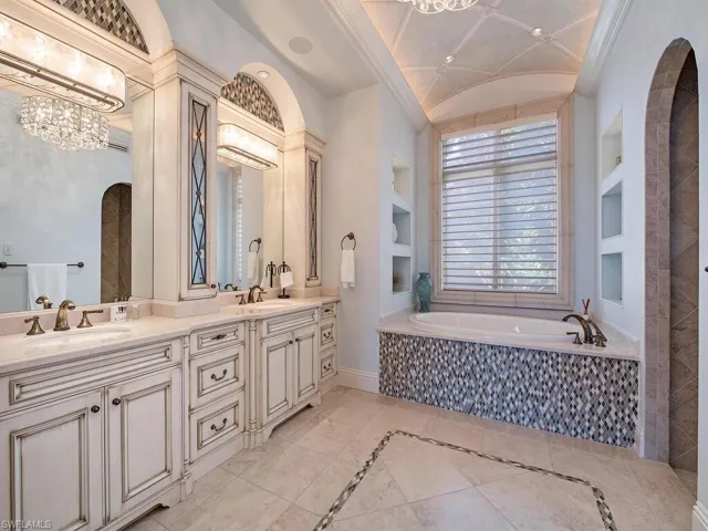 Bathroom with a relaxing tiled bath, oversized vanity, dual sinks, tile floors, and built in shelves