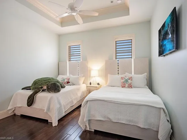 Bedroom with dark hardwood / wood-style floors, ceiling fan, a tray ceiling, and crown molding