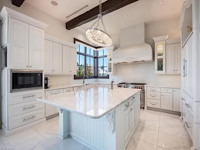 Kitchen featuring custom exhaust hood, beam ceiling, double oven range, black microwave, and a kitchen island with sink