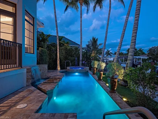 Pool at dusk featuring pool water feature and an in ground hot tub