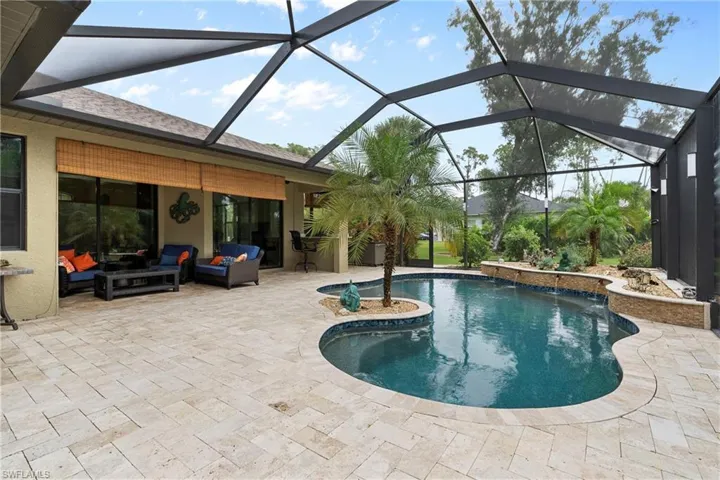 View of swimming pool featuring pool water feature, travertine patio, an outdoor living space, and a lanai