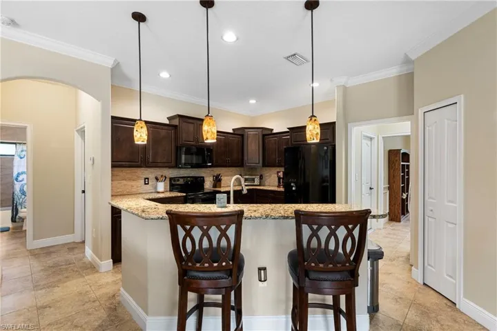 Kitchen featuring light stone counters, black appliances, dark brown cabinets, decorative light fixtures, and backsplash