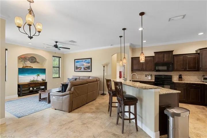 Kitchen with backsplash, a kitchen breakfast bar, a center island with sink, hanging light fixtures, and black appliances