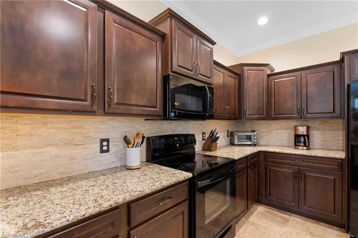 Kitchen featuring dark brown cabinetry, backsplash, black appliances, light stone countertops, and crown molding