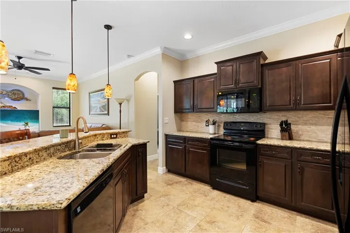 Kitchen with sink, a center island with sink, black appliances, crown molding, and decorative backsplash