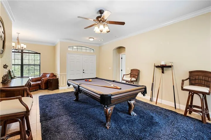 Living with ceiling fan with notable chandelier, ornamental molding, light tile patterned flooring, and billiards
