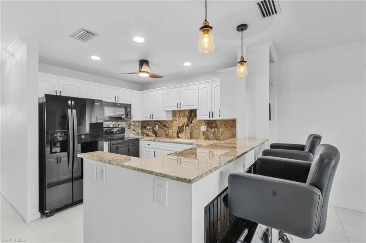 Kitchen with kitchen peninsula, backsplash, black appliances, pendant lighting, and white cabinetry