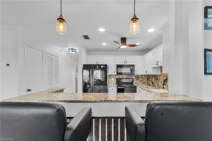 Kitchen with black appliances, white cabinetry, sink, and pendant lighting