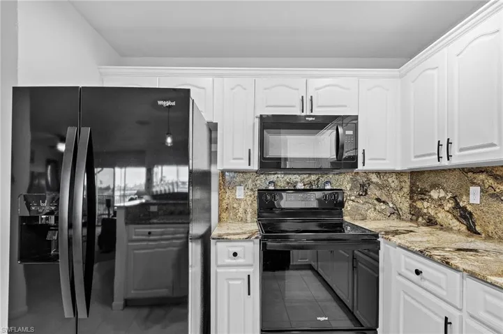 Kitchen featuring tasteful backsplash, tile patterned flooring, white cabinets, and black appliances