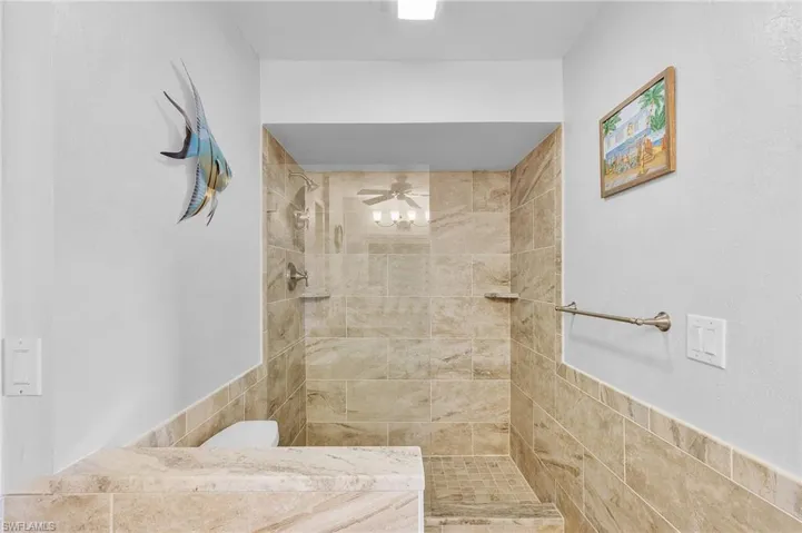 Bathroom featuring a tile shower, ceiling fan, tile walls, and toilet