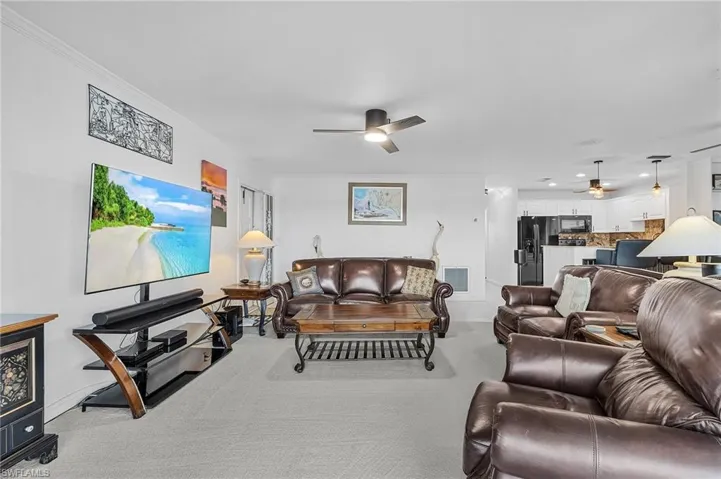 Carpeted living room featuring crown molding and ceiling fan