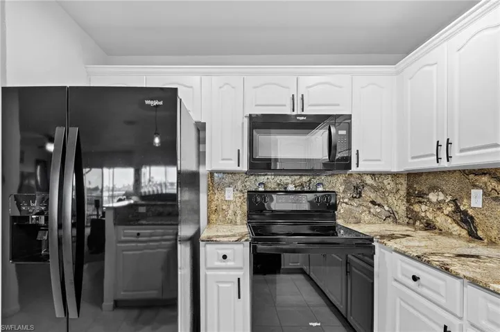 Kitchen featuring backsplash, white cabinetry, dark tile patterned floors, and black appliances