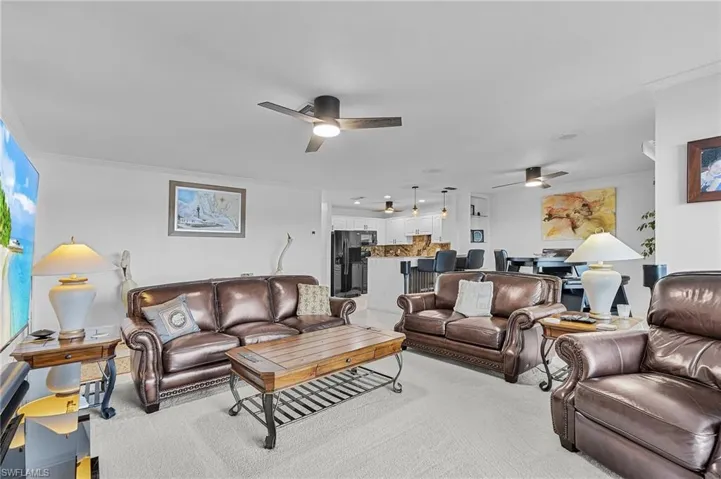 Carpeted living room with ceiling fan and crown molding
