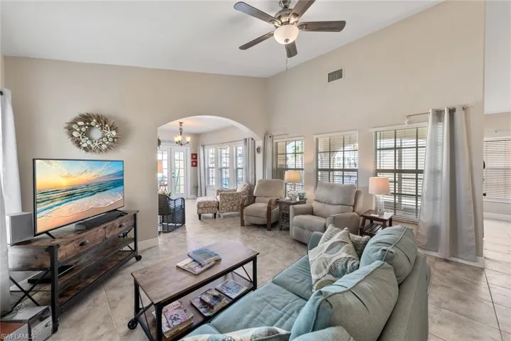 Tiled living area with visible vents, baseboards, a ceiling fan, arched walkways, and lofted ceiling