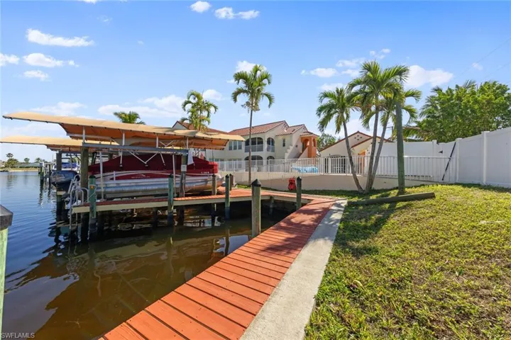 View of dock with a water view, fence, boat lift, and a yard