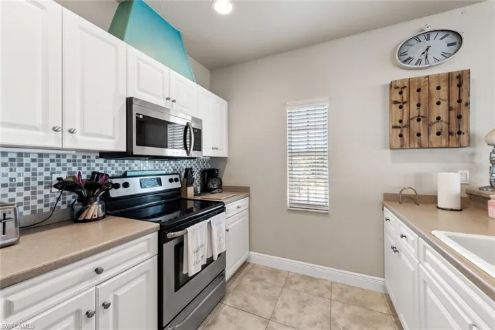 Kitchen with backsplash, white cabinets, light tile patterned flooring, and appliances with stainless steel finishes